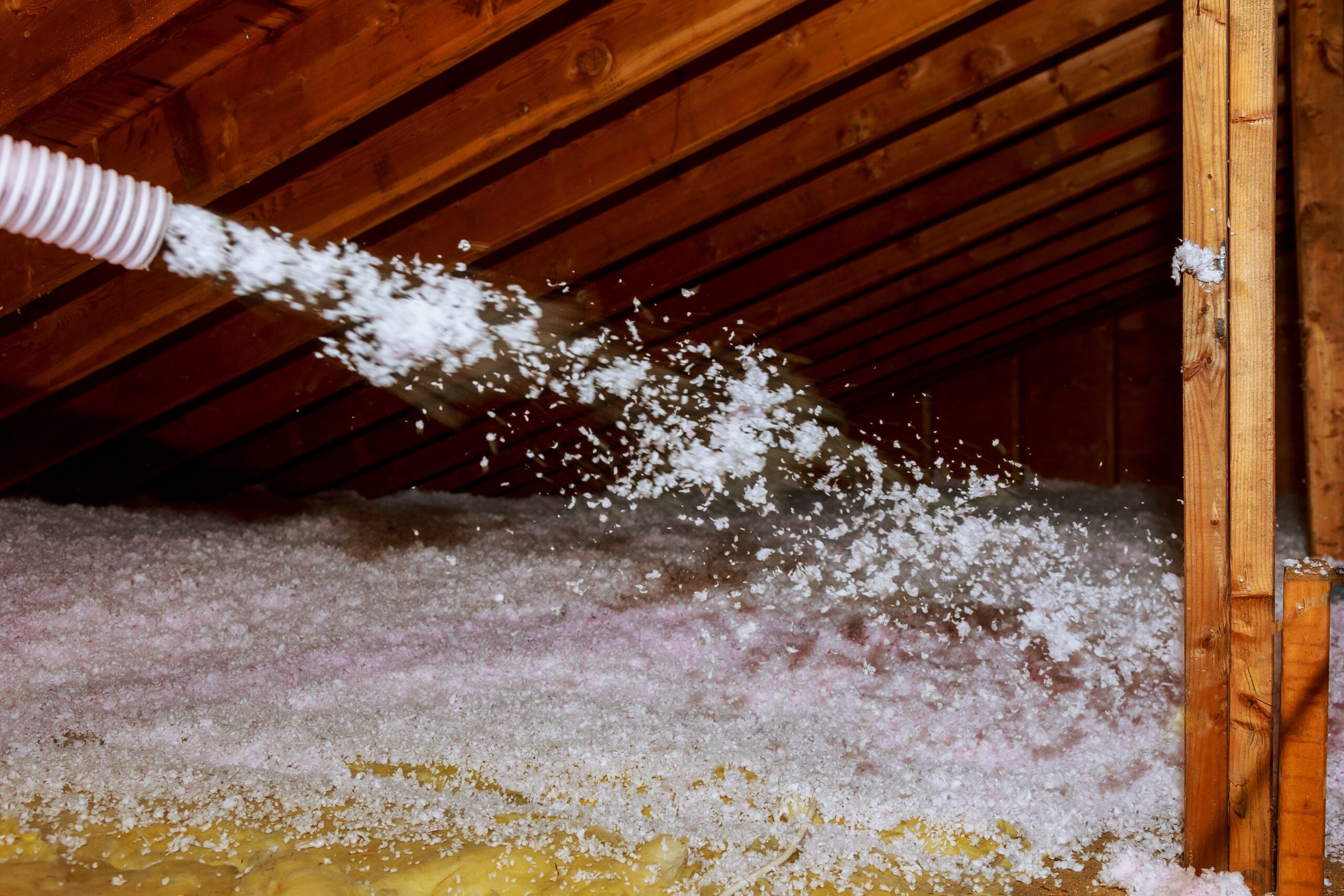Worker Spraying mineral rock wool of thermal insulation layer under the roof house attic insulation