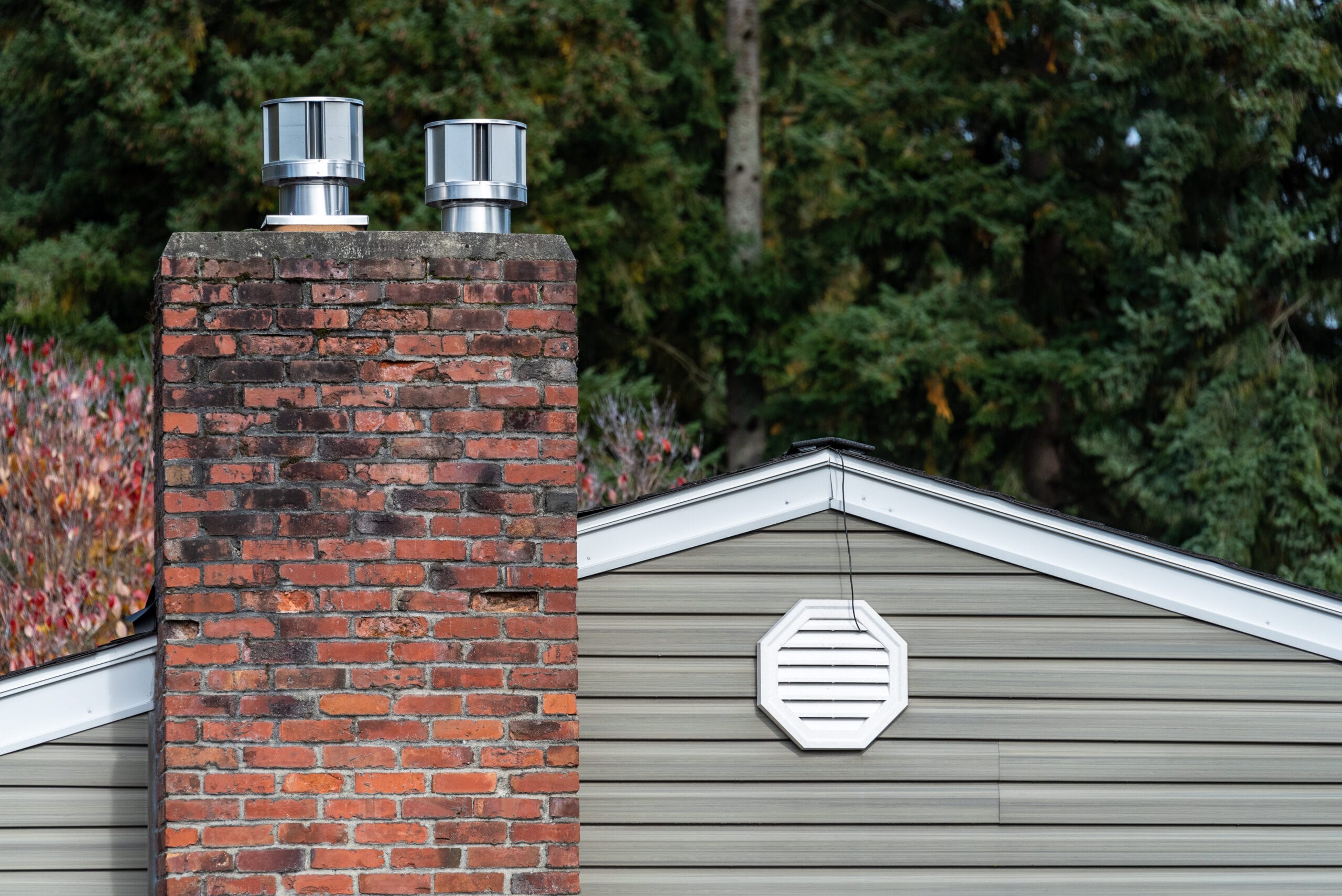Exterior wall of suburban house, old brick chimney with chimney vents, attic gable fan exhaust vent on wall